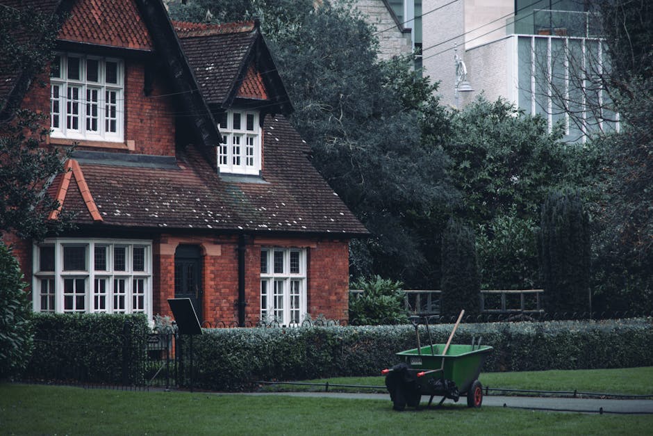 A red brick house with a steeply pitched roof covered in dark tiles, featuring small white-framed bay windows on the ground floor and a pair of similar windows on the upper floor, set within a well-ma